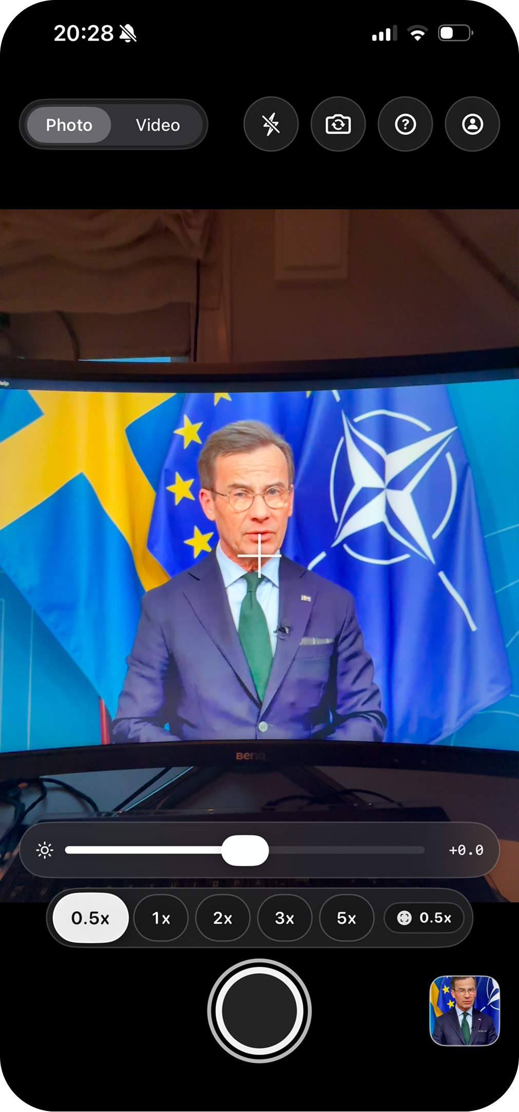 RealRec 0.5x zoom verification frame showing a monitor, desk, and room context around a politician video
